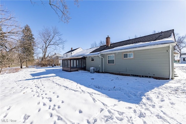 snow covered rear of property with central AC and a sunroom