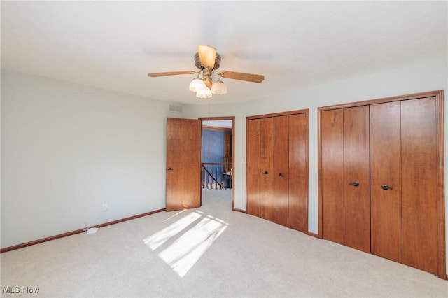 unfurnished bedroom with light carpet, two closets, and ceiling fan