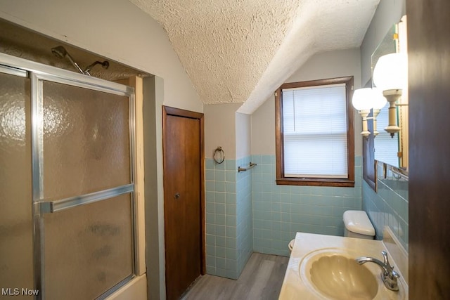 bathroom featuring vaulted ceiling, wood-type flooring, tile walls, vanity, and a textured ceiling