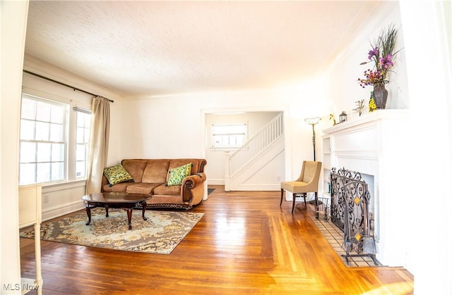 living room with a tile fireplace, wood-type flooring, ornamental molding, and a textured ceiling