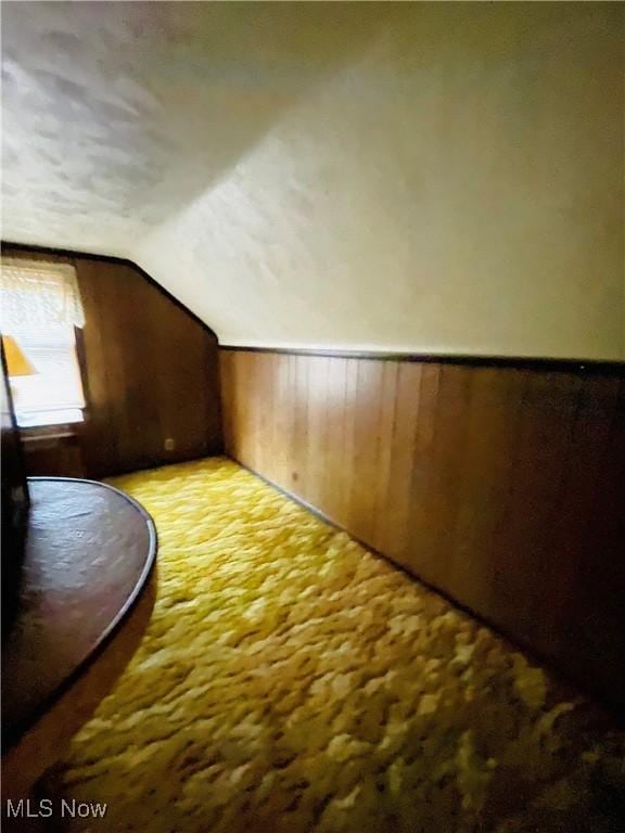 additional living space featuring vaulted ceiling and wood walls