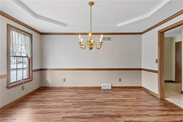 unfurnished dining area featuring an inviting chandelier, a tray ceiling, ornamental molding, and light wood-type flooring