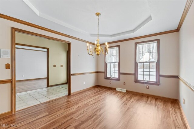 spare room with a chandelier, ornamental molding, a raised ceiling, and light hardwood / wood-style floors