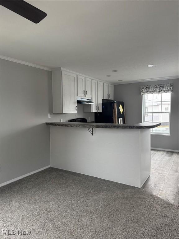 kitchen with white cabinetry, a kitchen bar, kitchen peninsula, crown molding, and black fridge