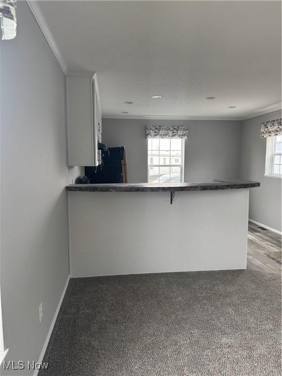 kitchen with crown molding, fridge, kitchen peninsula, carpet, and white cabinets