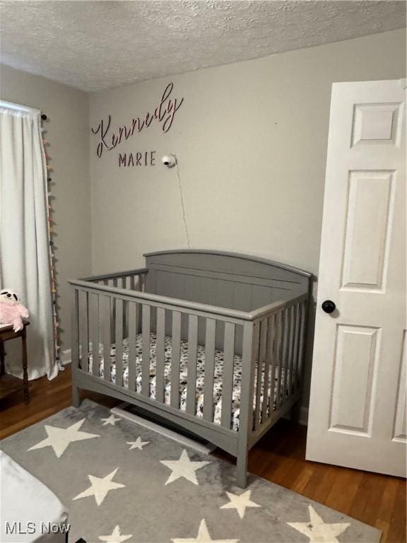 bedroom featuring a nursery area, dark hardwood / wood-style floors, and a textured ceiling