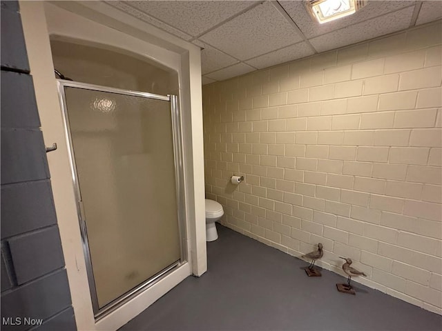 bathroom featuring a shower with door, a paneled ceiling, concrete flooring, and toilet