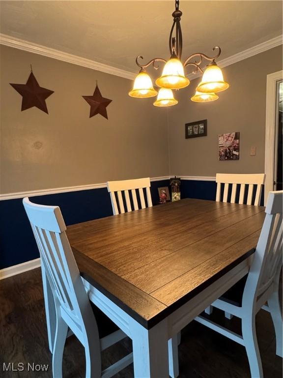 unfurnished dining area featuring dark wood-type flooring, ornamental molding, and a chandelier