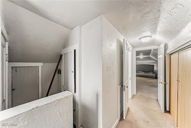 corridor with vaulted ceiling, light colored carpet, and a textured ceiling