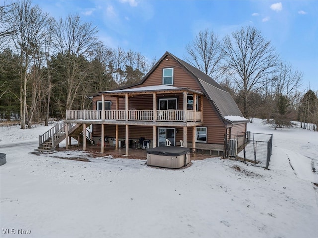 snow covered rear of property featuring a hot tub, a deck, and central air condition unit