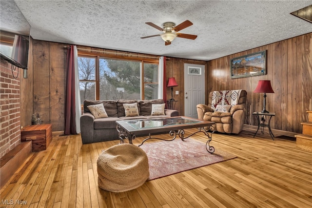 living room with ceiling fan, light hardwood / wood-style flooring, wooden walls, and a textured ceiling