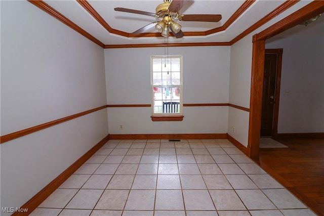 empty room with ceiling fan, ornamental molding, a tray ceiling, and light tile patterned floors