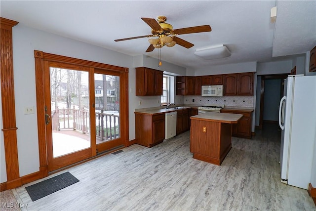 kitchen featuring white appliances, light hardwood / wood-style flooring, ceiling fan, backsplash, and a center island