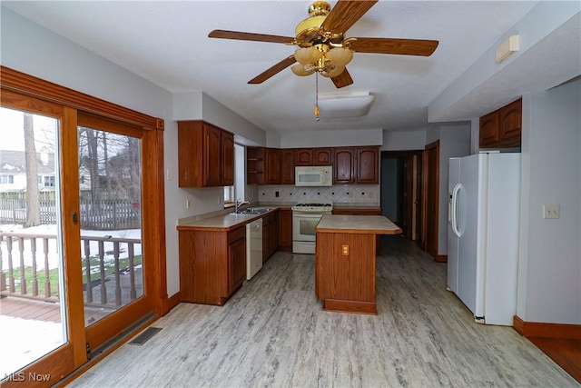 kitchen with sink, a center island, white appliances, light hardwood / wood-style floors, and backsplash