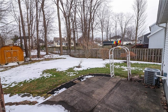 yard covered in snow featuring a playground, a patio, central air condition unit, and a storage shed