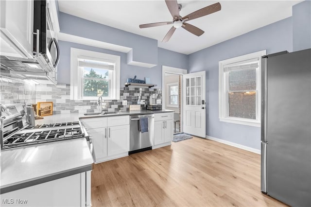 kitchen featuring appliances with stainless steel finishes, white cabinetry, sink, decorative backsplash, and light wood-type flooring