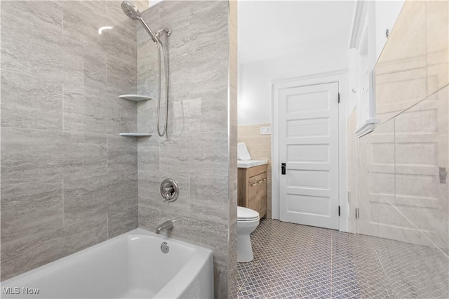 full bathroom featuring tile walls, vanity, tiled shower / bath, tile patterned floors, and toilet