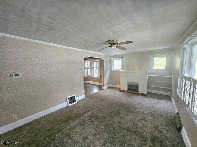 unfurnished living room featuring a textured ceiling, ornamental molding, dark carpet, ceiling fan, and a fireplace