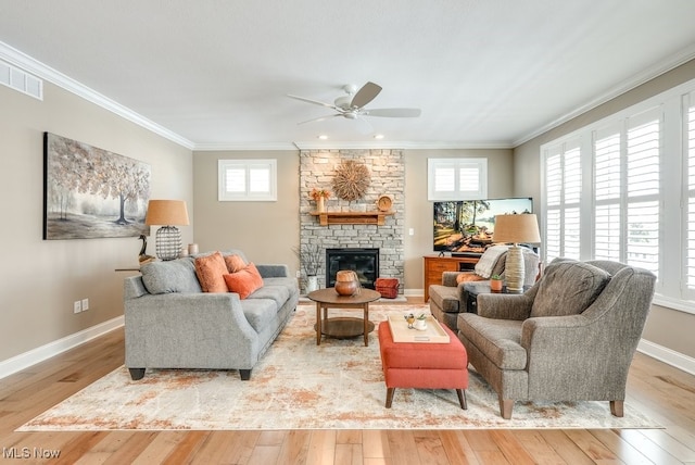 living room with crown molding, a stone fireplace, ceiling fan, and light wood-type flooring