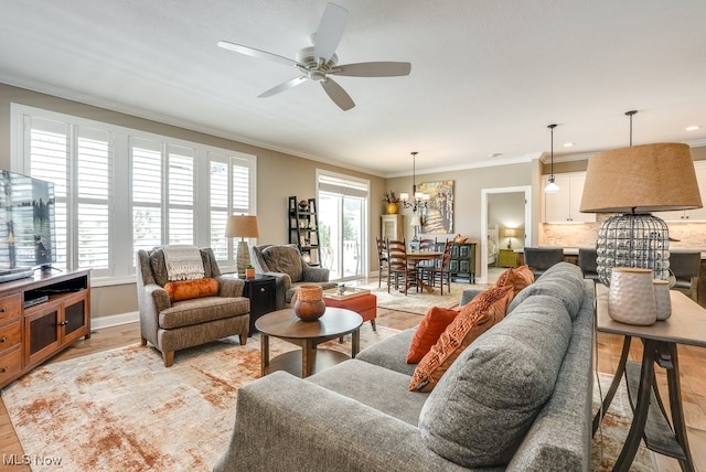 living room with crown molding, ceiling fan with notable chandelier, and light hardwood / wood-style floors