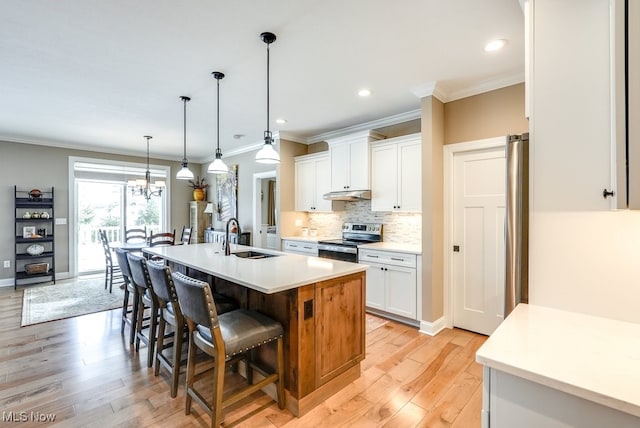 kitchen featuring decorative light fixtures, white cabinetry, sink, stainless steel appliances, and a center island with sink