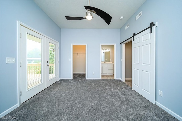 unfurnished bedroom featuring french doors, a spacious closet, access to outside, dark carpet, and a barn door