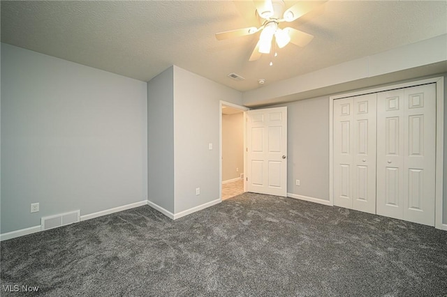 unfurnished bedroom featuring ceiling fan, a closet, a textured ceiling, and dark colored carpet