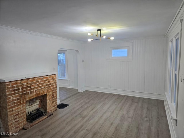 unfurnished living room featuring ornamental molding, a notable chandelier, a fireplace, and light hardwood / wood-style floors