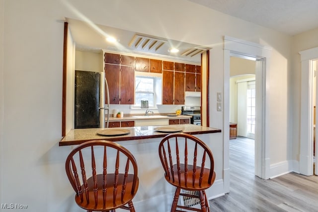 kitchen featuring sink, appliances with stainless steel finishes, a kitchen bar, kitchen peninsula, and light wood-type flooring