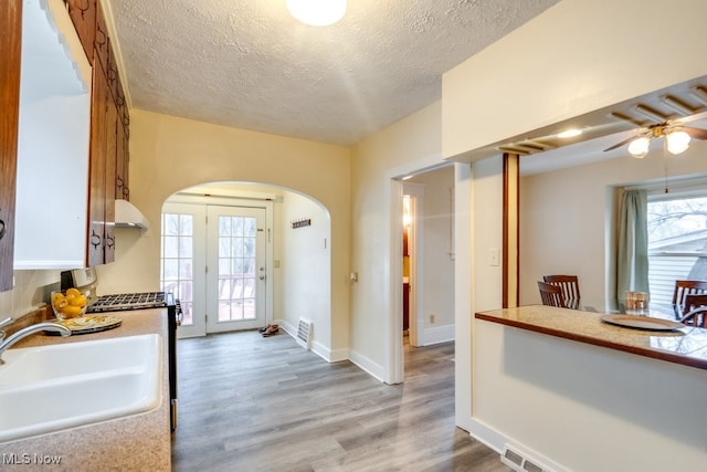 kitchen featuring sink, light hardwood / wood-style floors, white cabinets, a textured ceiling, and gas range