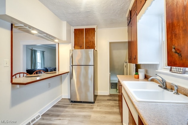 kitchen featuring sink, stainless steel fridge, a textured ceiling, and light wood-type flooring