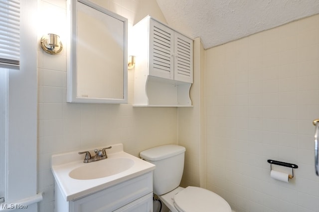 bathroom featuring vanity, tile walls, toilet, and a textured ceiling