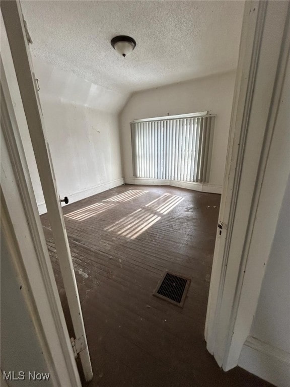 unfurnished room featuring dark hardwood / wood-style floors, vaulted ceiling, and a textured ceiling