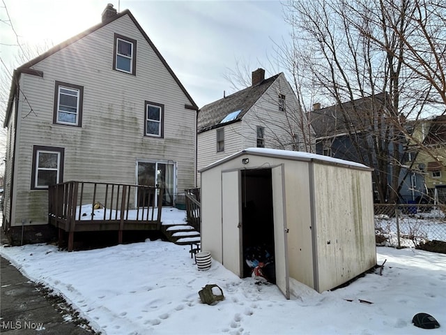 snow covered house featuring a wooden deck and a storage unit