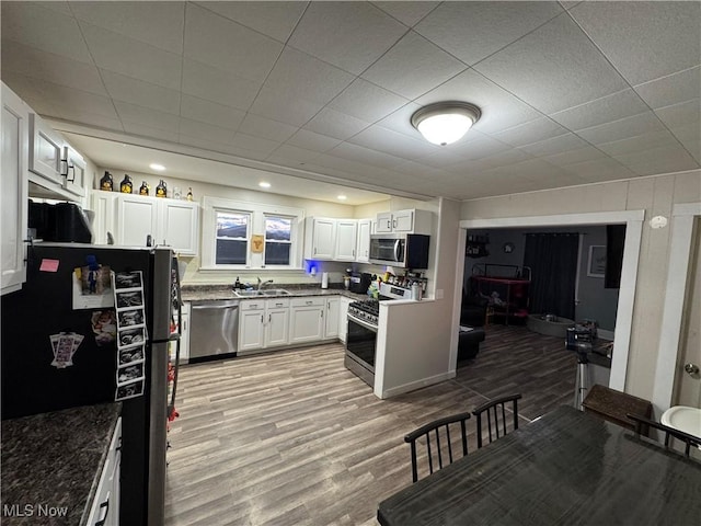 kitchen with sink, dark stone countertops, stainless steel appliances, light hardwood / wood-style floors, and white cabinets