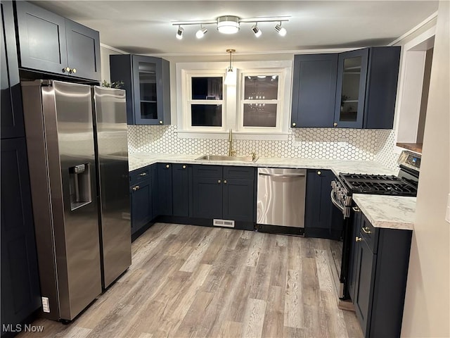 kitchen with sink, appliances with stainless steel finishes, hanging light fixtures, tasteful backsplash, and light wood-type flooring