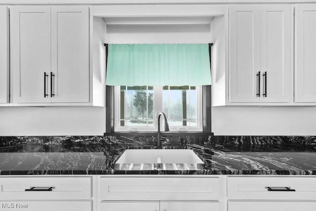 kitchen featuring white cabinetry, sink, and dark stone counters