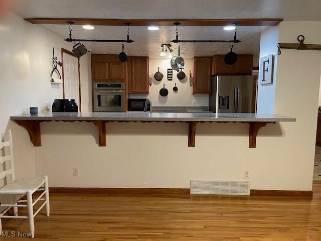 kitchen with appliances with stainless steel finishes, light wood-type flooring, a kitchen breakfast bar, and decorative light fixtures