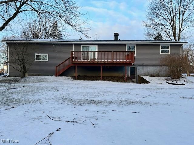 snow covered back of property with a deck