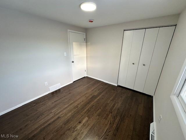 unfurnished bedroom with dark hardwood / wood-style flooring and a closet