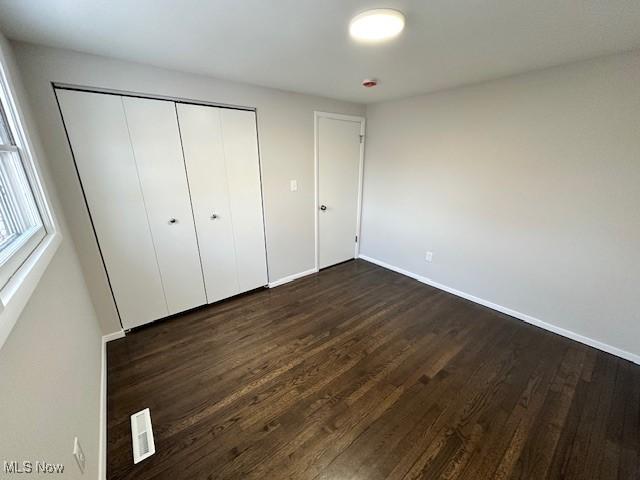 unfurnished bedroom with dark hardwood / wood-style floors and a closet