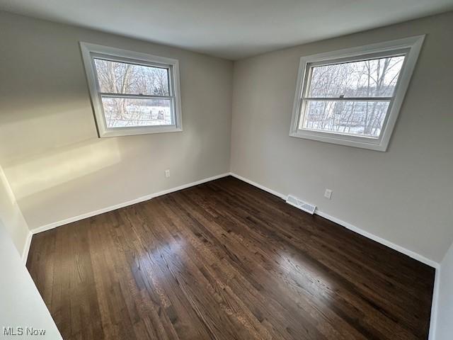 empty room with a wealth of natural light and dark hardwood / wood-style flooring