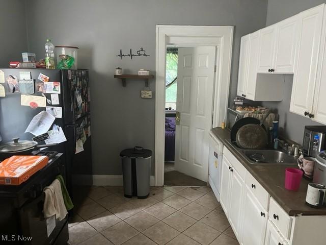 kitchen with white cabinetry, black fridge, sink, and light tile patterned floors