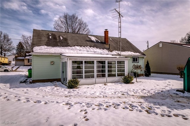 snow covered back of property with a sunroom