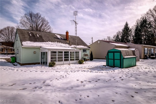 snow covered property with a storage shed and a sunroom