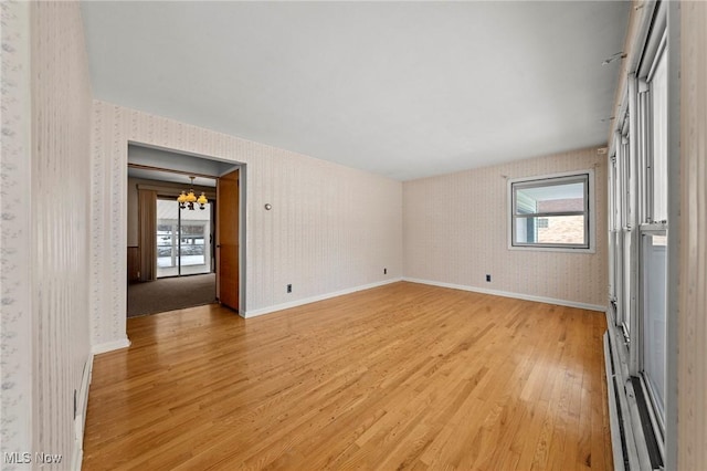 empty room with an inviting chandelier, light hardwood / wood-style flooring, a baseboard radiator, and a healthy amount of sunlight