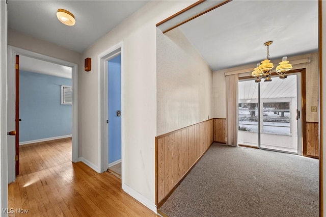 hall featuring wood-type flooring, wooden walls, and a chandelier