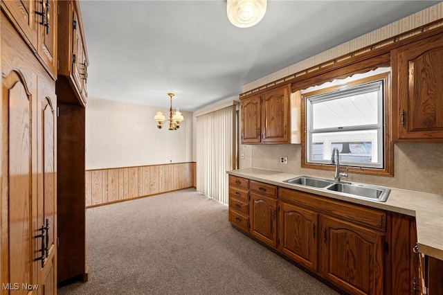 kitchen with sink, hanging light fixtures, carpet floors, a chandelier, and wood walls