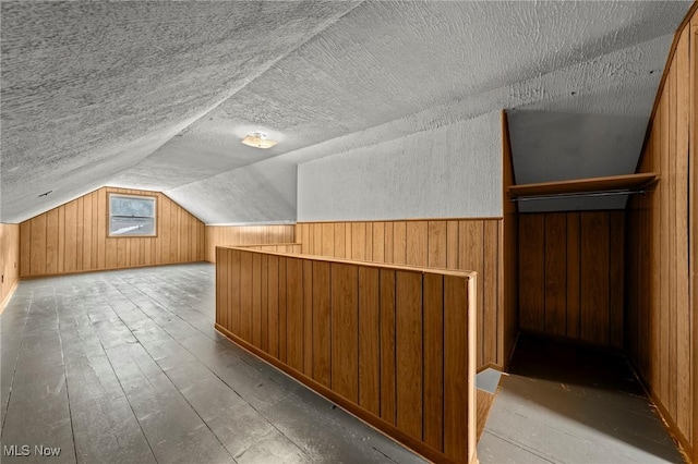 additional living space featuring hardwood / wood-style flooring, vaulted ceiling, a textured ceiling, and wood walls