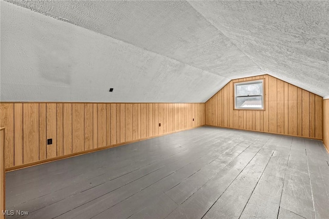 bonus room featuring lofted ceiling, hardwood / wood-style flooring, wooden walls, and a textured ceiling